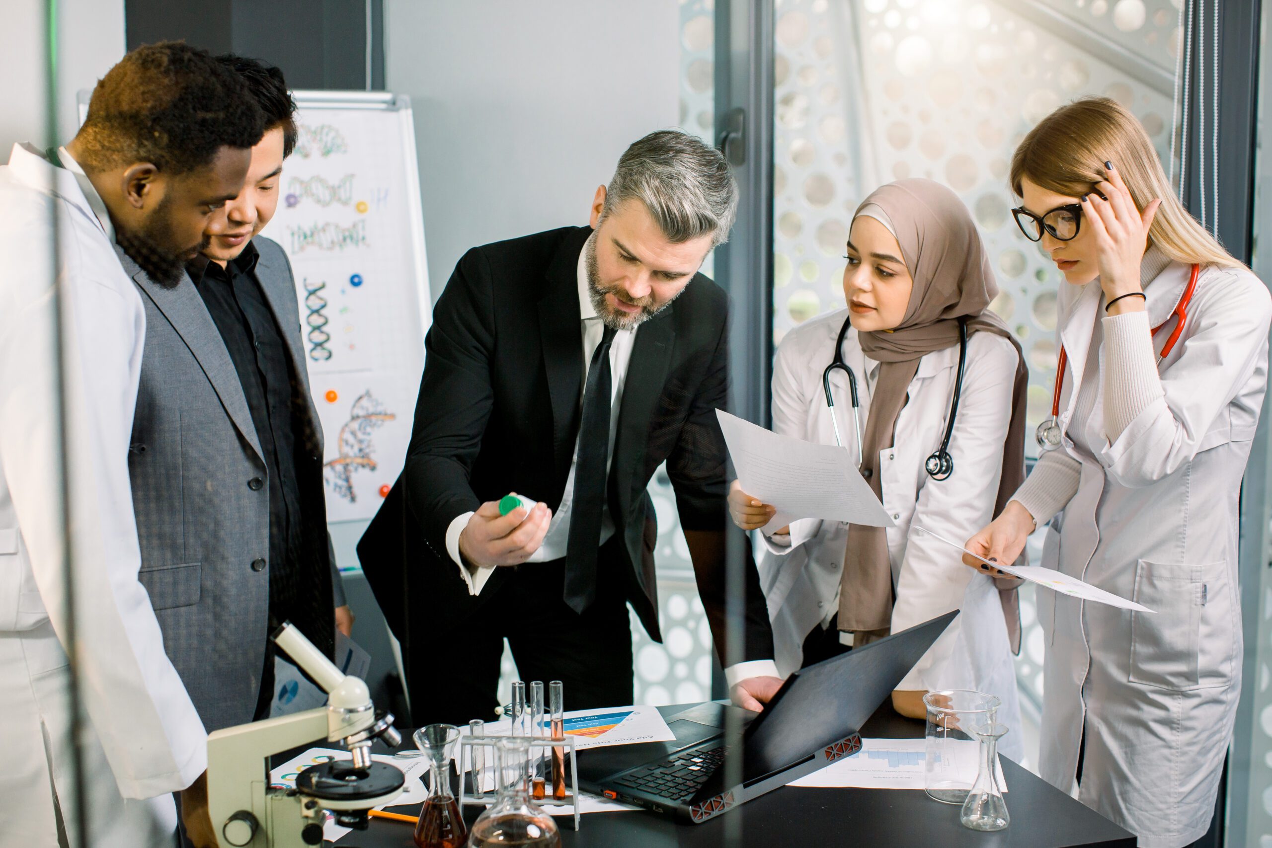 Image, Mature man in suit, pharmaceutical company director, holding a bottle with new medicine drug, smiling, while talking with multiethnic team of doctors researchers, about clinical trial